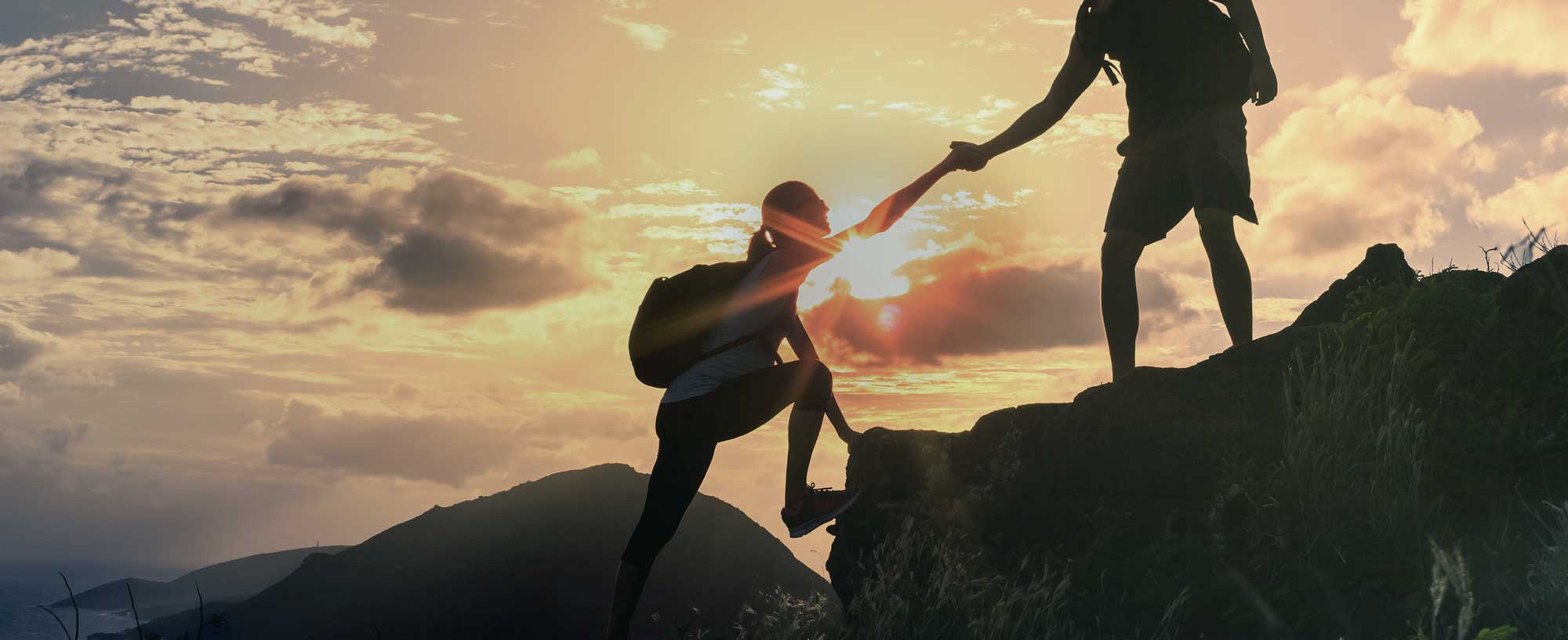 Zwei Wanderer erklimmen einen Berg vor einem Sonnenuntergang
